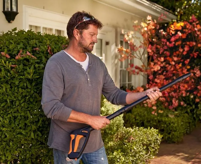 Man holding a pressure-washer lance beside a house